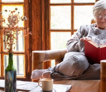 une senior en train de lire sur son fauteuil dans son chalet en bois habitat idéal pour senior