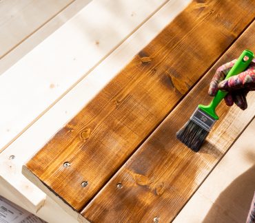 pinceau tenu par une main sur des planches en bois pour illustrer l'entretient de son chalet en bois